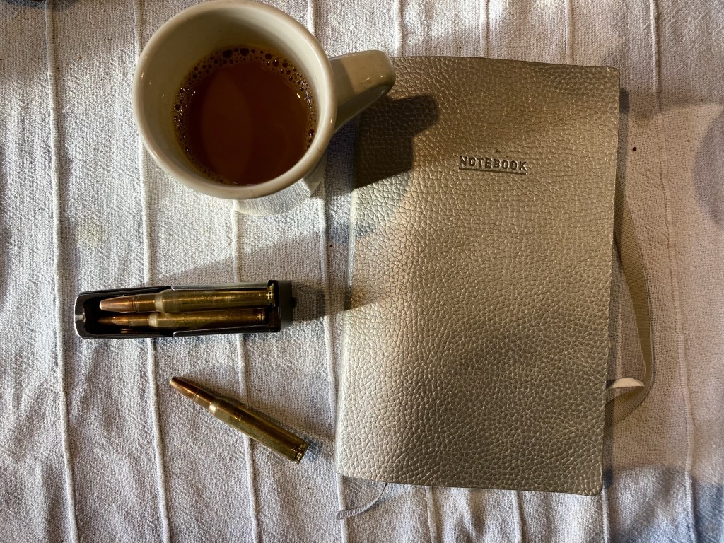 Coffee mug, notebook and bullet casings on a table, photographed from above
